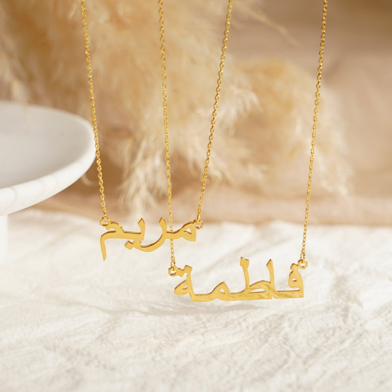 Gold name necklace with Arabic script on a textured surface

