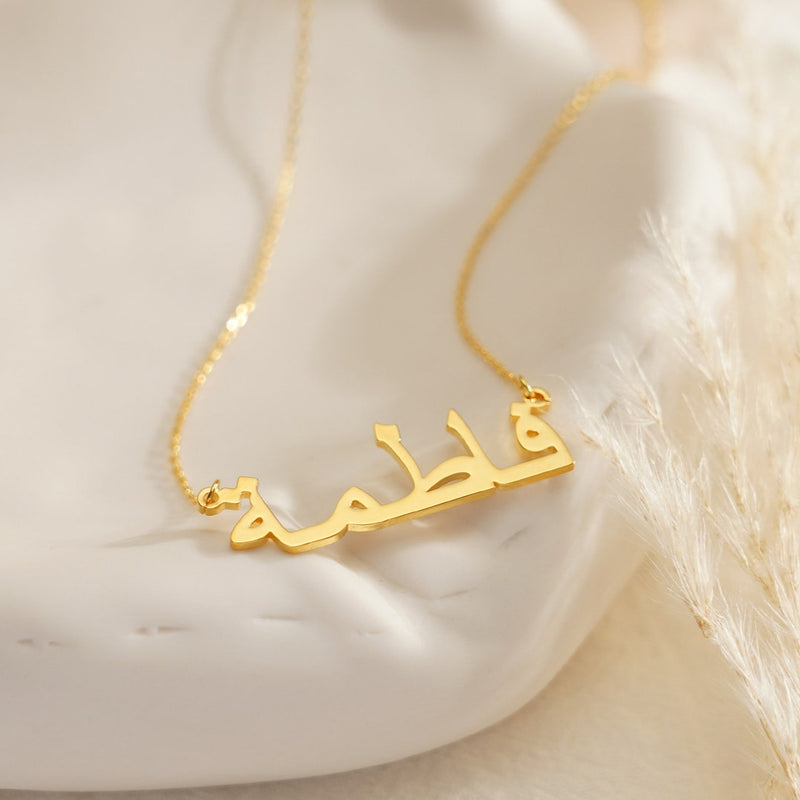 Gold necklace with Arabic script on a soft white background

